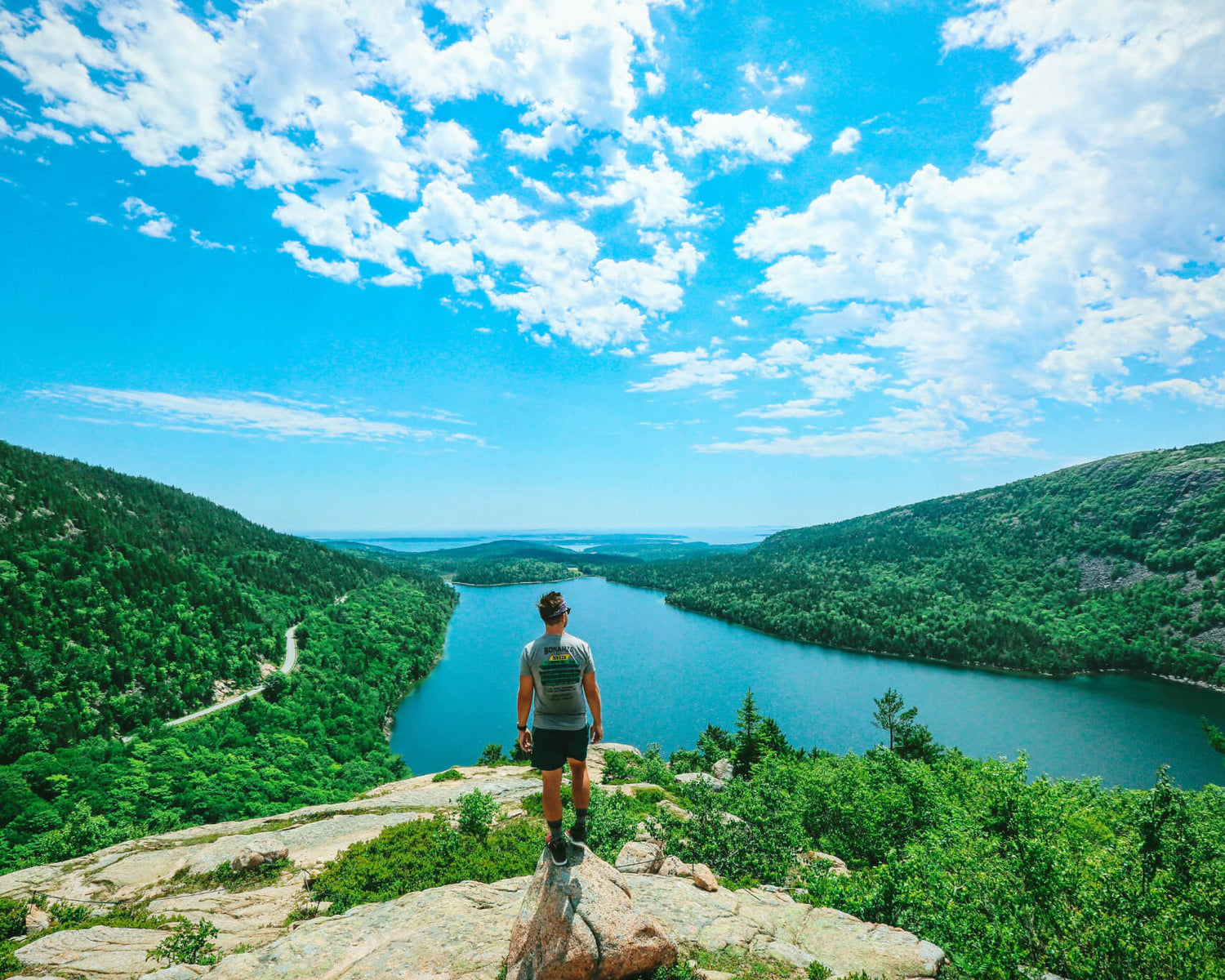 Person standing on rocky mountain peak overlooking mountains and ponds